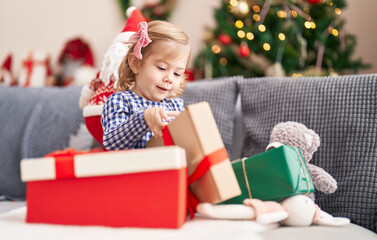 Obraz na płótnie Canvas Adorable hispanic girl holding gift sitting on sofa by christmas tree at home
