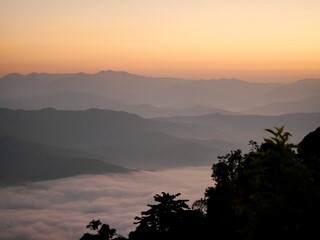 The mist flows through the mountain forest, Sun shining into tropical forest, Mist drifts through mountain ridges in the morning, slow floating fog blowing cover on the top of mountain 