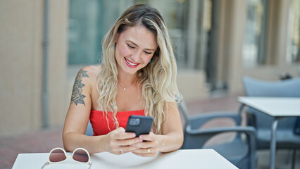 Young blonde woman using smartphone smiling at coffee shop terrace
