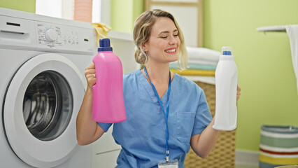 Young blonde woman professional cleaner holding detergent bottles at laundry room