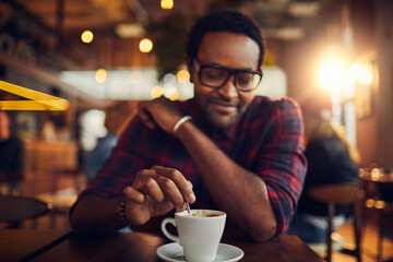 Young man sitting in cafe stirring or mixing a coffee mug