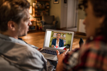 Young couple talking to their financial advisor over a video call on their laptop in the living room of their home