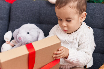 Adorable hispanic toddler unpacking christmas gift sitting on sofa at home