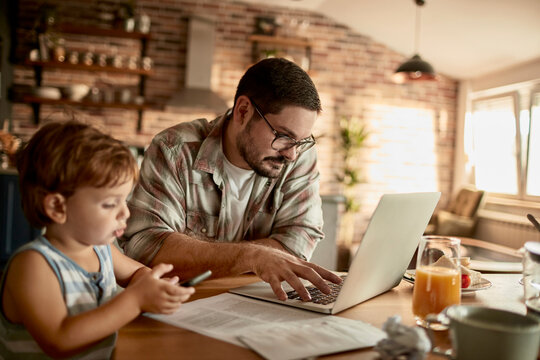 Father working on laptop with little son by his side at home