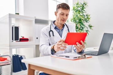 Young man doctor using touchpad sitting on table at clinic