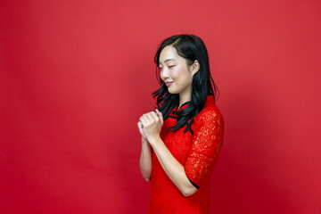 Asian chinese woman with red cheongsam or qipao doing polite respectful gesture for wishing the...