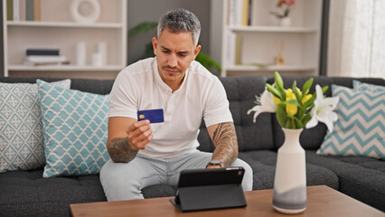 Young hispanic man shopping with touchpad and credit card at home