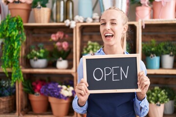 Young caucasian woman working at florist holding open sign winking looking at the camera with sexy...