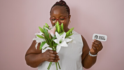 Confident african american woman joyfully smelling flower bouquet, over pink isolated background,...