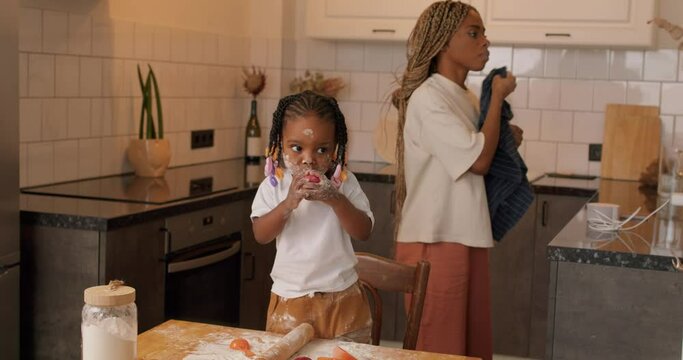funny little girl with flour on her face eating apple, while her mother wiping , cleanong her face with towel in the background, slow motion free spare time lifestyle