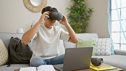 Young hispanic teenager studying on sofa, immersed in virtual reality while using laptop indoors