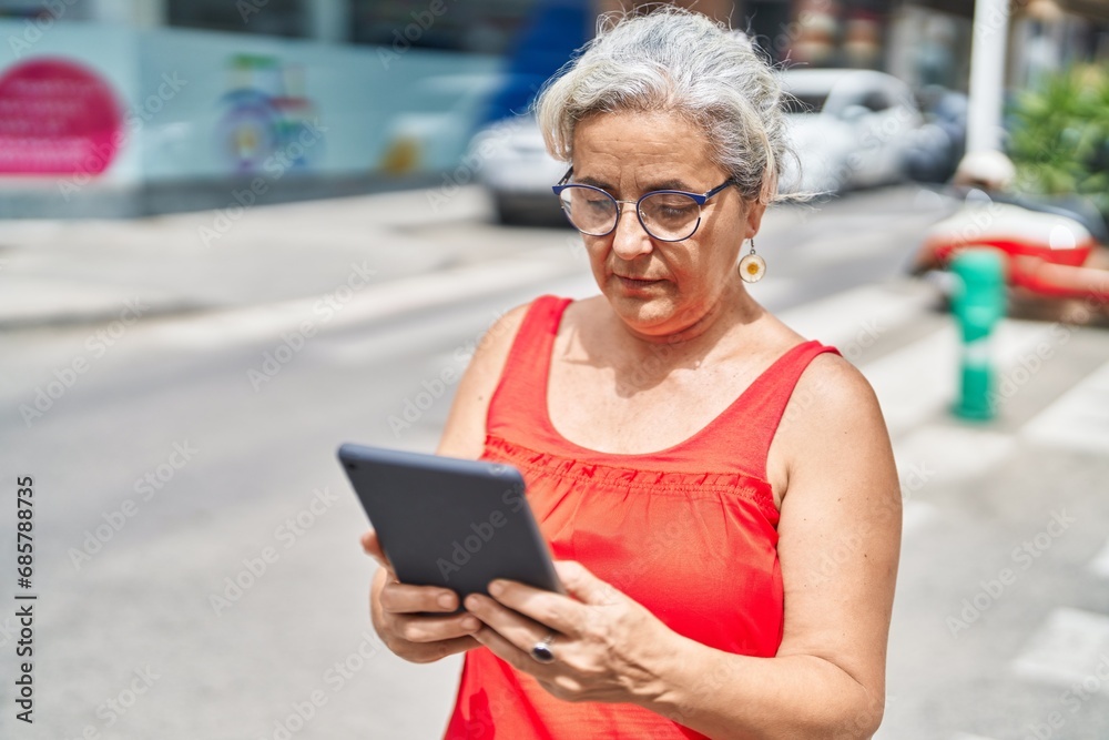 Poster Middle age grey-haired woman using touchpad with serious expression at street