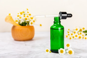 Glass bottle with chamomile essential oil on an old wooden background. Chamomile flowers, close up. Aromatherapy, spa and herbal medicine ingredients. Beauty concept.Copy space. Natural cosmetic