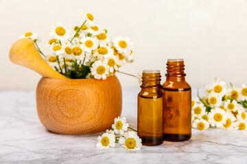 Glass bottle with chamomile essential oil on an old wooden background. Chamomile flowers, close up....