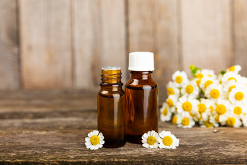 Glass bottle with chamomile essential oil on an old wooden background. Chamomile flowers, close up. Aromatherapy, spa and herbal medicine ingredients. Beauty concept.Copy space. Natural cosmetic