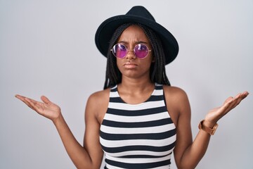 Young african american with braids wearing hat and sunglasses clueless and confused expression with...