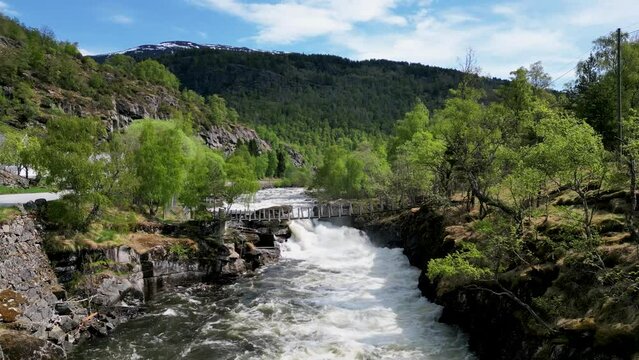 River with footpath wooden bridge in Norwegian mountain and woodland area. Lærdal River filmed by drone in 4K.