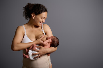 New mother feeds her newborn baby with breast milk, for healthy growth, smiling isolate on gray...