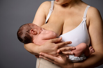 Selective focus on a 2 week old adorable newborn baby suckling at his mother's breast, isolated...
