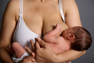 Close-up view of a 2 week old adorable newborn baby suckling at his mother's breast, isolated gray studio background