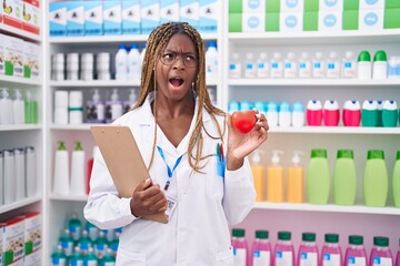 African american woman with braided hair working at pharmacy drugstore angry and mad screaming...