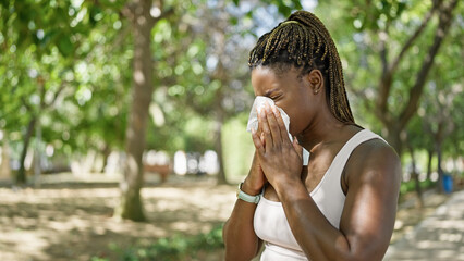 African american woman using tissue with pollen allergy at park - obrazy, fototapety, plakaty