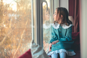 a pensive cute girl sits and looks out the window