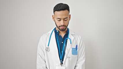 Young hispanic man doctor standing with serious expression looking down over isolated white background © Krakenimages.com