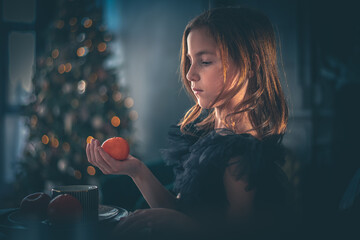 a cute girl in a black dress sits at a table with tangerine. holiday, new year, christmas