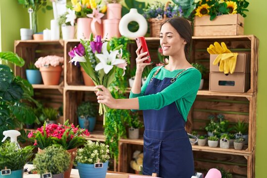 Young beautiful hispanic woman florist make photo to flower by smartphone at flower shop