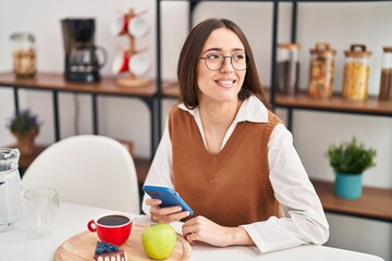 Young beautiful hispanic woman having breakfast using smartphone at home