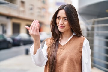 Young beautiful hispanic woman smiling confident doing coming gesture with hand at street