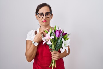 Middle age brunette woman wearing apron working at florist shop holding bouquet pointing aside worried and nervous with forefinger, concerned and surprised expression