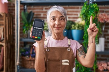 Middle age woman with tattoos working at florist shop holding dataphone smiling with an idea or...