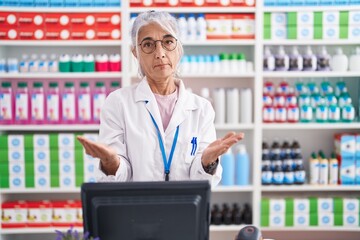 Middle age woman with tattoos working at pharmacy drugstore clueless and confused with open arms,...