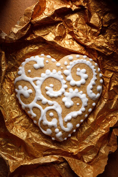 Gingerbread heart decorated with white icing on a golden background, close up view. Traditional Christmas cookie