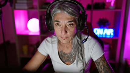 Mature, grey-haired woman gamer, in serious gaming mode, streaming live in the heart of the night from her cozy home gaming room, sporting headphones and a mic © Krakenimages.com