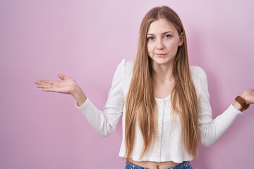 Young caucasian woman standing over pink background clueless and confused expression with arms and hands raised. doubt concept.