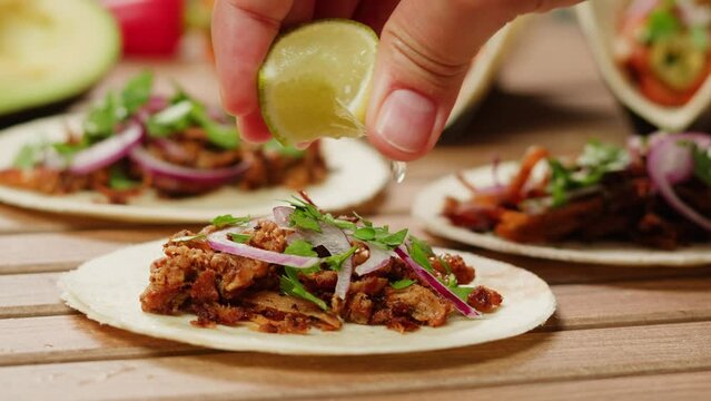 Traditional mexican food tacos with onion and cilantro on the top close-up. Squeezing lime on homemade tacos with meat and vegetables 