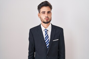 Young hispanic man with tattoos wearing business suit and tie looking at the camera blowing a kiss...