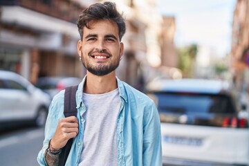 Young hispanic man student smiling confident wearing backpack at street