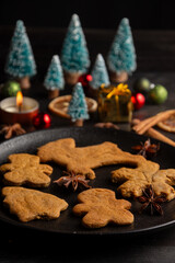 Top view of plate with gingerbread cookies with cinnamon, star anise, orange, Christmas trees and candle, black background, vertical, with copy space