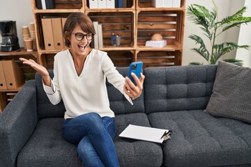 Brunette woman doing online session at consultation office celebrating victory with happy smile and winner expression with raised hands