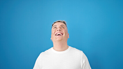 Young caucasian man looking up with surprise expression over isolated blue background