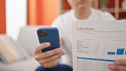 Young caucasian man using smartphone reading document at home