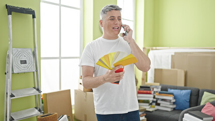 Young caucasian man holding color test talking on smartphone at new home