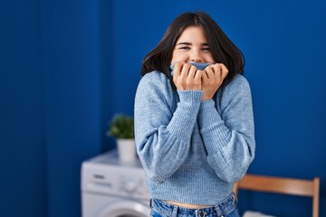 Young beautiful hispanic woman smelling sweater standing at laundry room