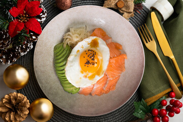 Teriyaki salmon donburi with fried egg, avocado, onion, red pepper and other vegetables. Christmas food served on a table decorated with Christmas motifs.