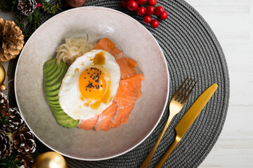 Teriyaki salmon donburi with fried egg, avocado, onion, red pepper and other vegetables. Christmas food served on a table decorated with Christmas motifs.