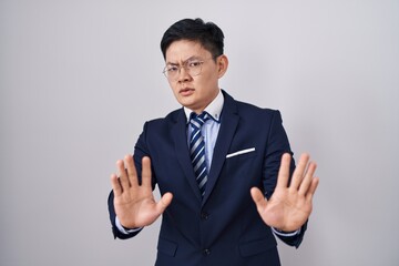 Young asian man wearing business suit and tie moving away hands palms showing refusal and denial...